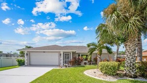 A single-story house with a garage, surrounded by a well-maintained lawn and palm trees. - 3-bedroom & den house in welcoming Cape Coral with Pool, centrally located!🌴 (Cape Coral)