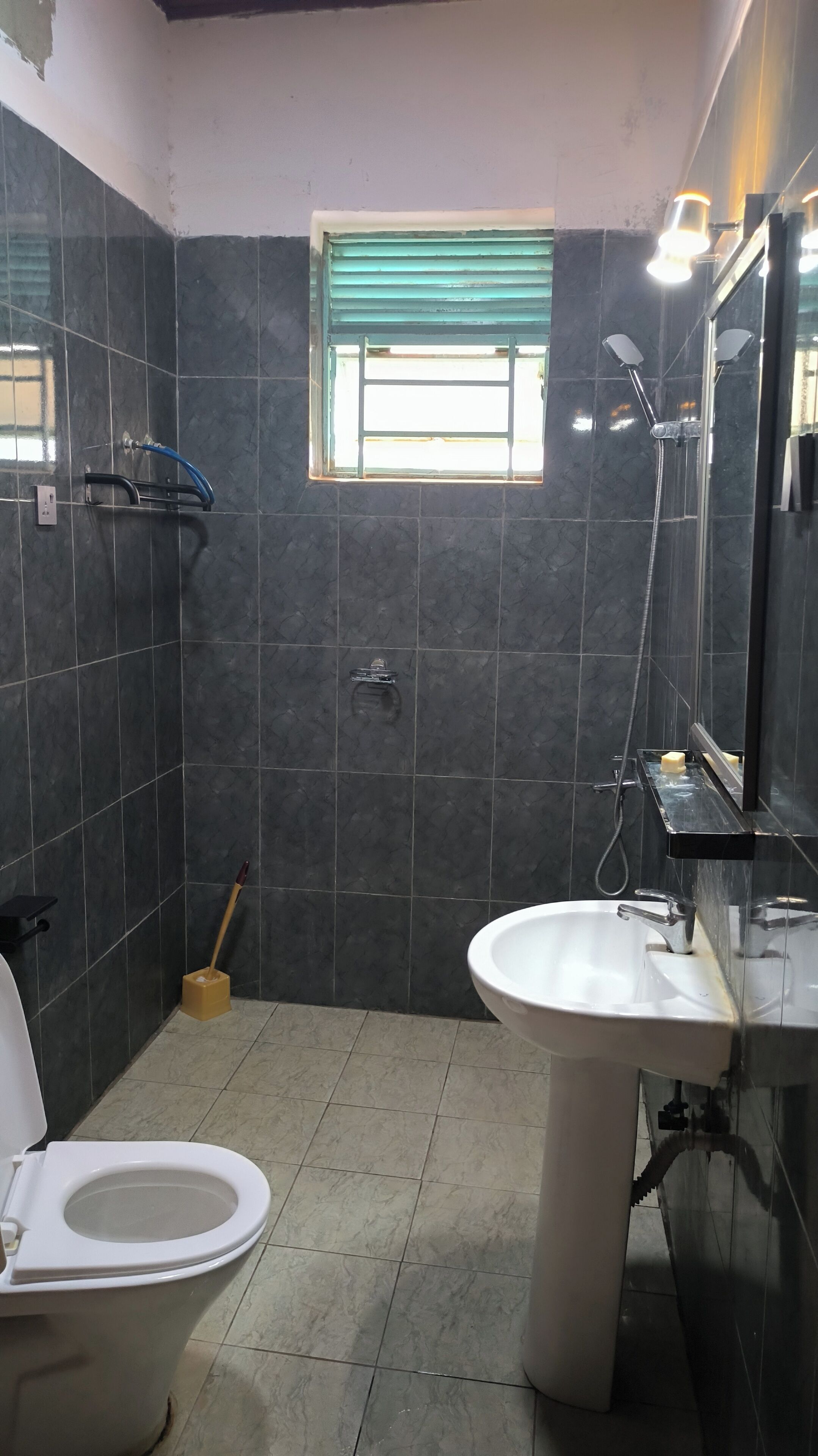 A bathroom with a toilet, sink, shower, and a window.