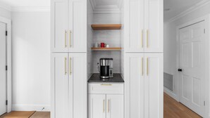 A kitchen with white cabinets, a coffee maker, and a red mug on a shelf. - Cozy North Fork Home Close to Beaches, Wineries, and Town, Perfect for Families (East Marion)