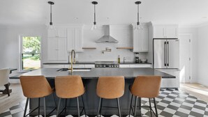 A modern kitchen with a central island, bar stools, stainless steel appliances, and pendant lighting. - Cozy North Fork Home Close to Beaches, Wineries, and Town, Perfect for Families (East Marion)