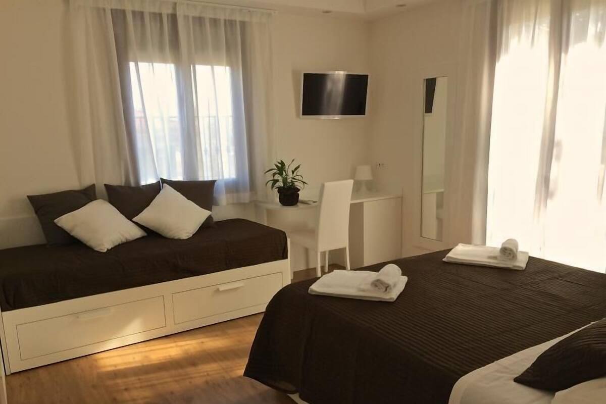Een hotelkamer met een bed, een bureau, een stoel, een televisie en een raam met gordijnen.