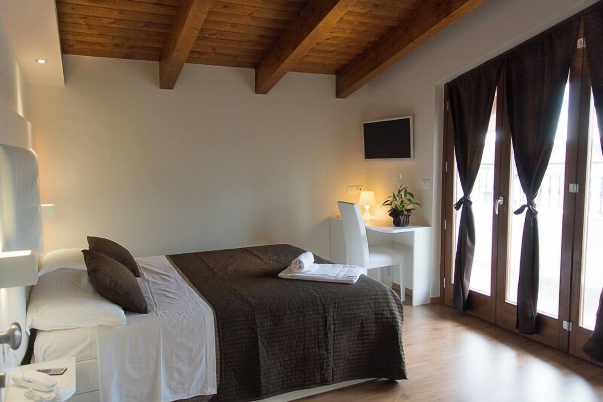 Een slaapkamer met een bed, nachtkastje, lamp en een bureau met stoel.