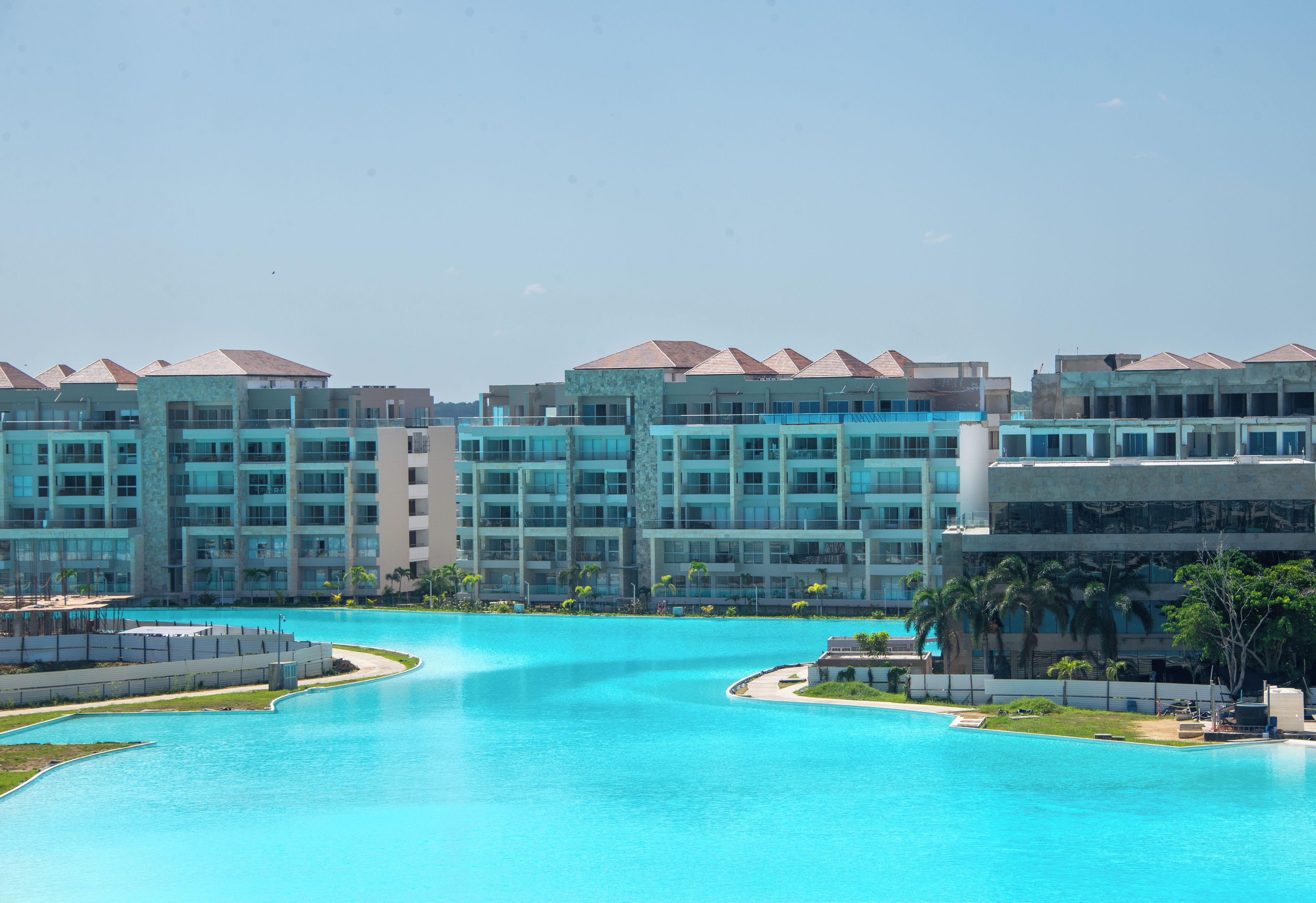 A resort with multiple buildings, a central swimming pool, and palm trees.