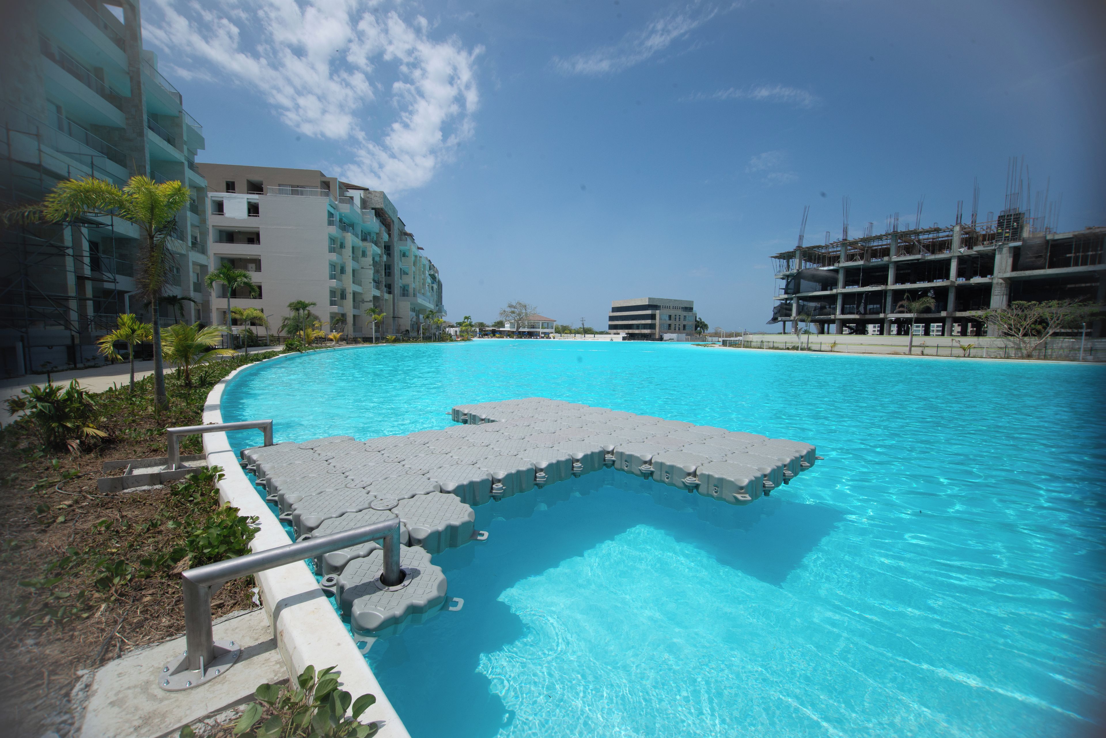 Une piscine dotée d’une terrasse intégrée, entourée de bâtiments modernes et de palmiers.