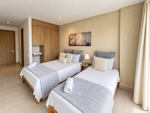 A hotel room with two beds, a wooden wardrobe, a painting on the wall, and a bathroom with a curtain. - Baia Kristal Prive | 2 Bedrooms | Sleeps 8 | P31L (Cartagena de Indias)
