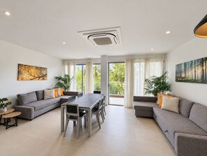 A modern living room with a grey sofa, a dining table, and a large window offering a view of greenery. - Baia Kristal Prive | 2 Bedrooms | Sleeps 8 | P31L (Cartagena de Indias)