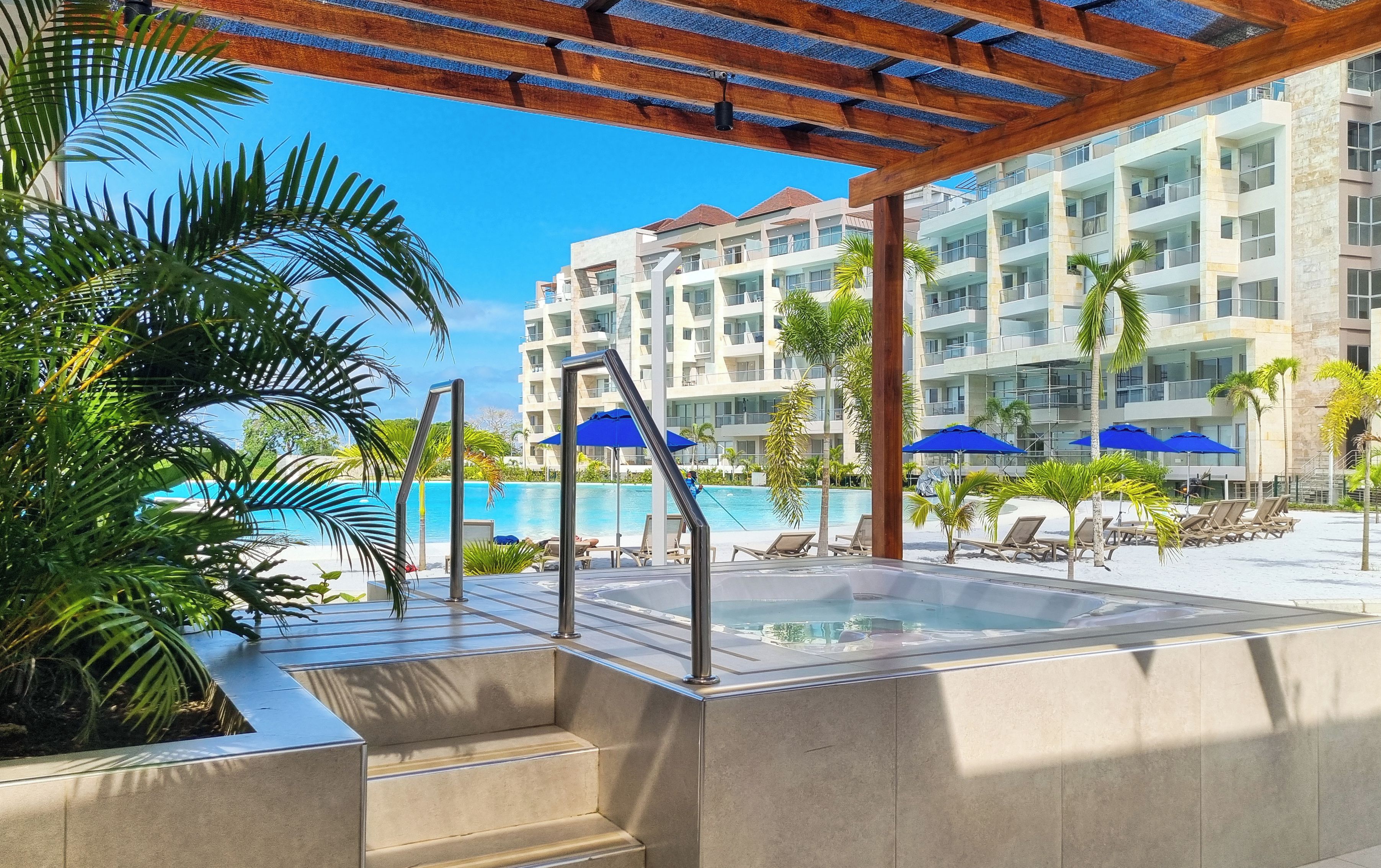 A pool area with a hot tub, lounge chairs, and umbrellas.
