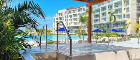 A pool area with a hot tub, lounge chairs, and umbrellas.