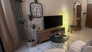 A living room with a television, a clock, a small table, and two chairs.