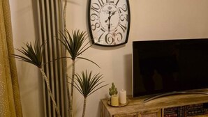 A wall-mounted clock, a television, and a wooden cabinet with books.