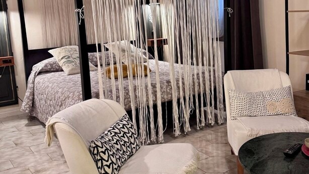 A bedroom with a four-poster bed, a macrame curtain, a sofa, and a small table.