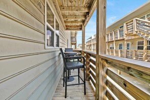 A wooden deck with a railing, a table, and two chairs. - Beachfront Condo Steps to Gulf Shores & Pool (Gulf Shores)