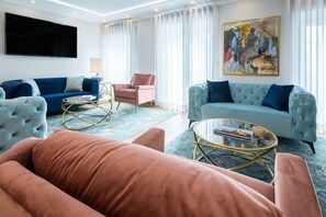 A modern living room with a blue sofa, a pink armchair, a tufted armchair, and a round coffee table.