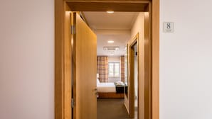 Un pasillo de hotel que lleva a una habitación con cama, ventana con cortinas y un letrero que indica el número 8.