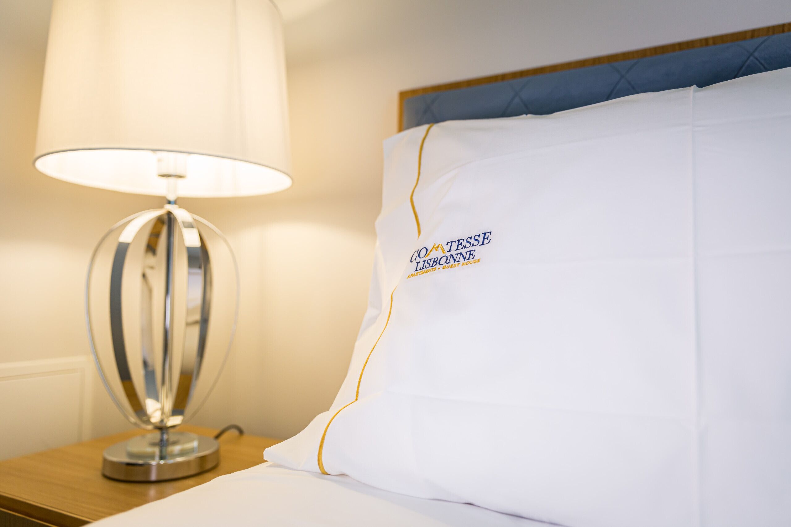 A neatly made bed with a white pillow featuring text, a round table lamp, and a wooden nightstand.