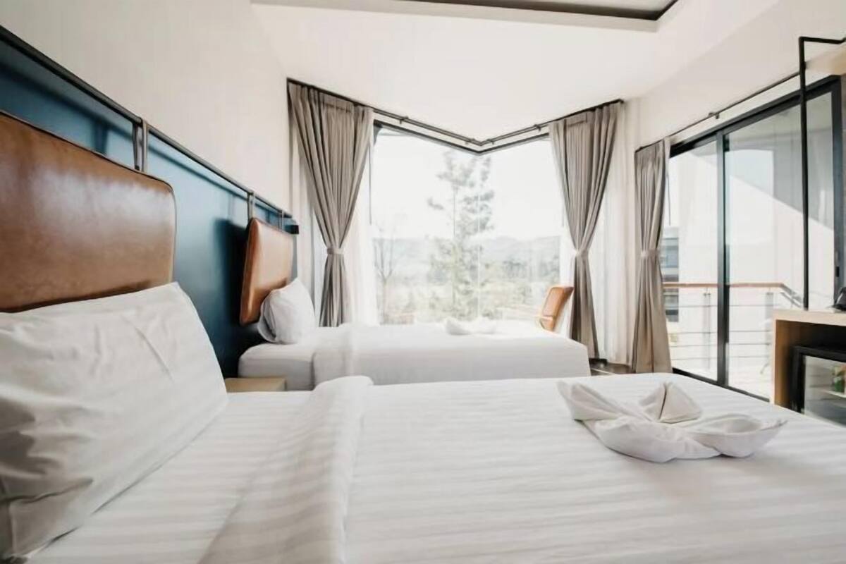 Ein Hotelzimmer mit zwei Betten, einem großen Fenster mit Vorhängen und Blick ins Freie.