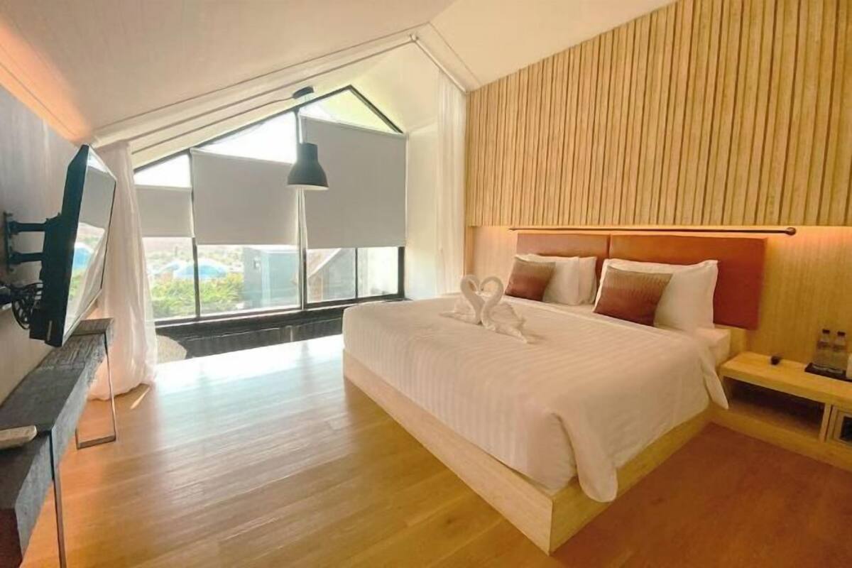 Ein modernes Hotelzimmer mit einem großen Bett, einem Schreibtisch, einem Sessel und Blick ins Freie.