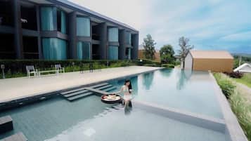 Piscina com um edifício moderno ao fundo, céu claro e algumas árvores.