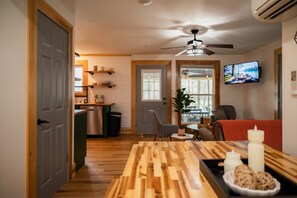 Una sala de estar acogedora con una mesa de comedor de madera, un televisor instalado en la pared y un ventilador de techo.