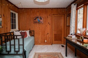 A cozy room with wooden walls, a bed with pillows, a desk with books, and a door.