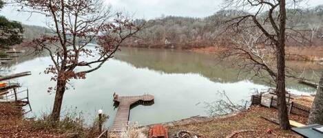 A lakeside view with a dock extending into the water, surrounded by trees and a wooden walkway.