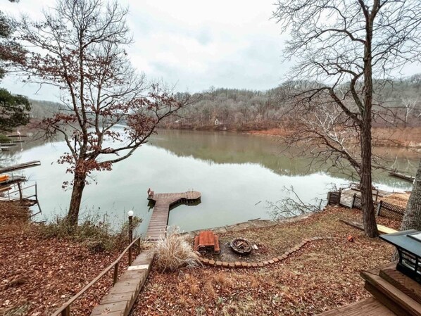 A lakeside view with a dock extending into the water, surrounded by trees and a wooden walkway.