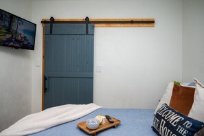 A bedroom with a bed, a wooden tray with a candle and remote, a blue blanket, a pillow with 'WELCOME TO THE HOUSE' text, and a sliding door. - Two lakefront cabins next door (Martinsville)