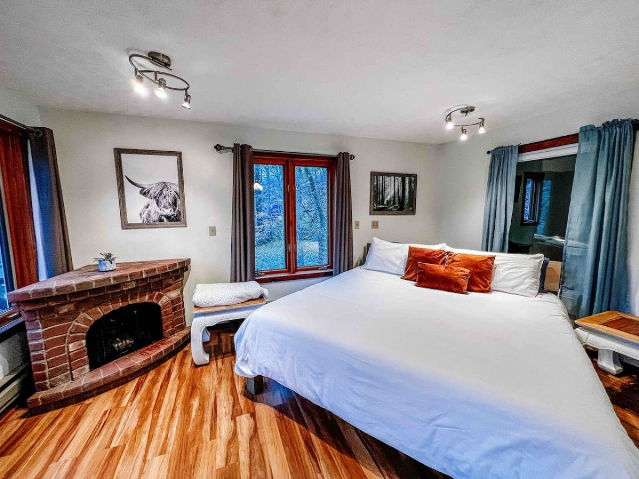 A bedroom with a large bed, a fireplace, a window with curtains, and a wooden floor.