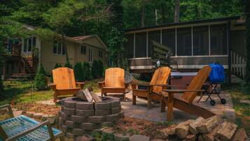 A backyard with a fire pit, wooden chairs, a grill, and a house in the background.