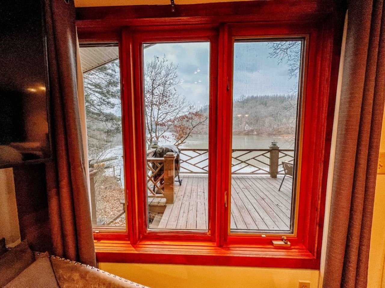 Een kamer met een groot raam dat uitkijkt op een houten terras met buitenmeubilair.