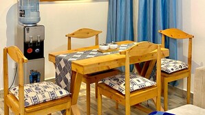 Una stanza con un tavolo e sedie in legno, un distributore d'acqua, un quadro e tende blu.