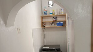 Una lavanderia con una lavatrice a carica frontale, uno scaffale con prodotti per la pulizia e un pavimento piastrellato.