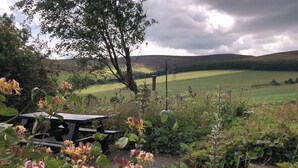 A picnic table surrounded by blooming flowers and a view of a green field and hills in the distance. - The Mill - Amazing spacious mountain escape in Speyside & the Cairngorms (Ballindalloch)