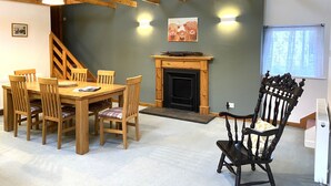 A dining area with a wooden table and chairs, a fireplace, and a staircase. - The Mill - Amazing spacious mountain escape in Speyside & the Cairngorms (Ballindalloch)