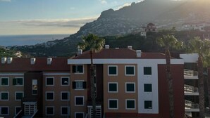 A coastal building with multiple balconies, a view of the sea, and a mountain in the background. - Ocean View Flat (Câmara de Lobos)