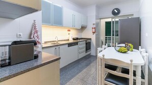 A compact kitchen with white cabinets, a dishwasher, a coffee machine, and a dining table with chairs. - Ocean View Flat (Câmara de Lobos)