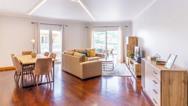 A modern living room with a wooden dining table, beige sofa, and a TV stand. - Ocean View Flat (Câmara de Lobos)