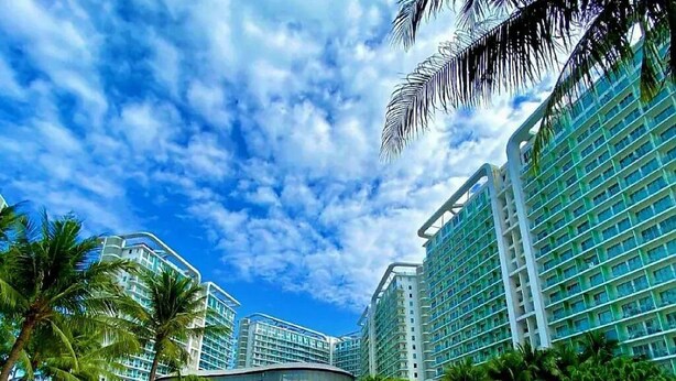 A resort with a pool, palm trees, and high-rise buildings. - Chic 2-bedroom condo with AC, WiFi in enchanting Parañaque (Parañaque)