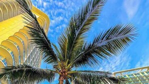 A hotel with a modern architectural design, featuring a prominent palm tree in the foreground and a large building with a curved facade in the background. - Chic 2-bedroom condo with AC, WiFi in enchanting Parañaque (Parañaque)
