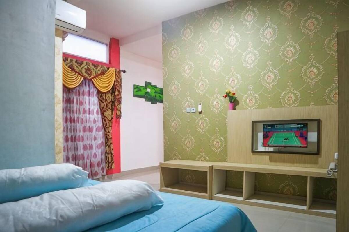 Um quarto com cama, televisão, estante e janela com cortinas.