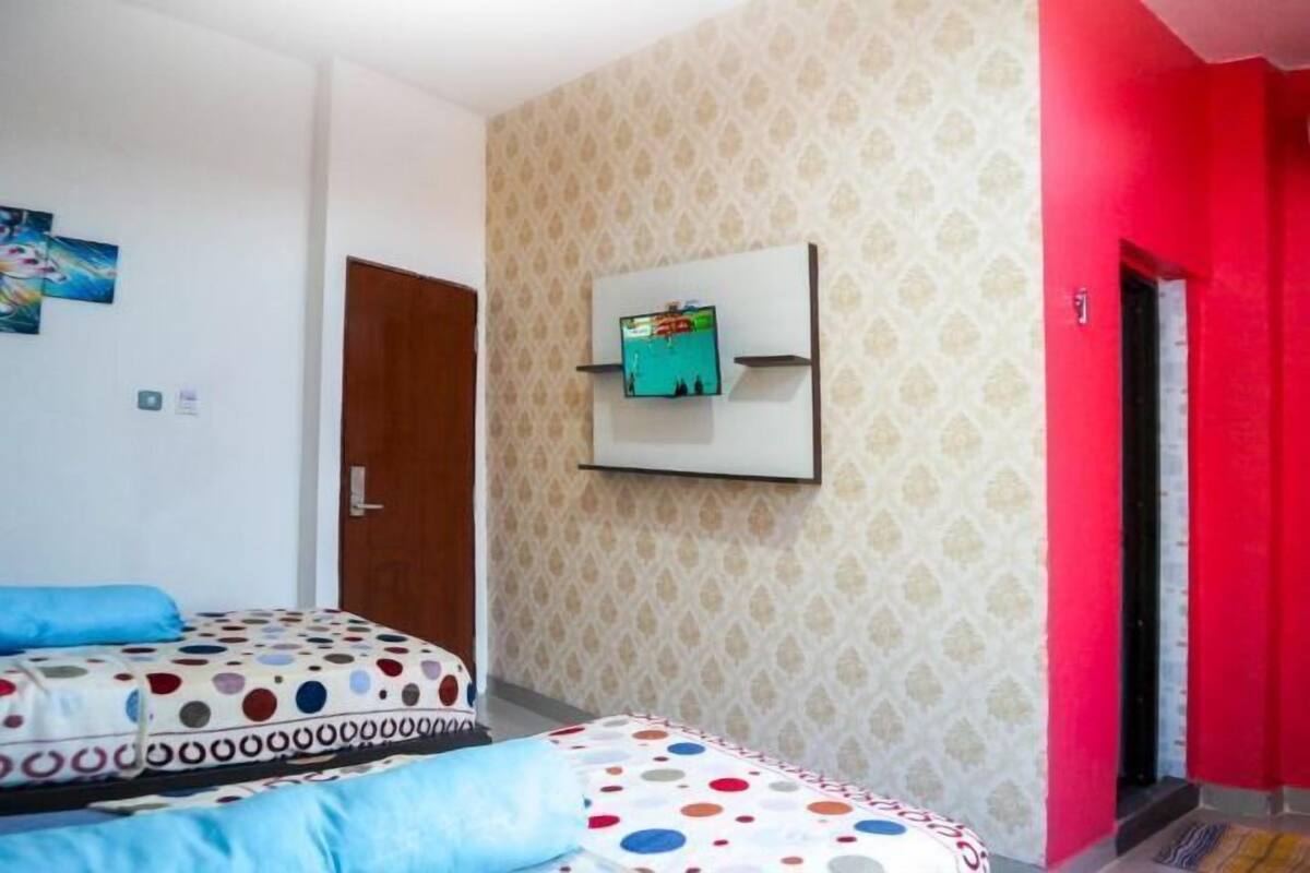 Quarto de hotel com duas camas, televisão presa na parede e papel de parede estampado.