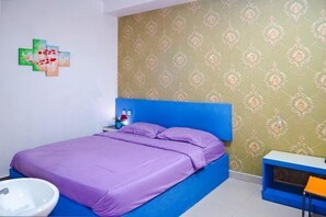 A bedroom with a bed, a nightstand, a small table, and a wall with patterned wallpaper. - Guest House Tunas Daud Near Universitas Kristen Artha Wacana Kupang Mitra RedDoorz (Kupang)