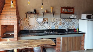 A kitchen with a brick oven, a wooden table, hanging light bulbs, and a microwave. - Villa da Serra chalé (Lima Duarte)