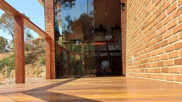 An outdoor deck with a glass door leading to a room. - Villa da Serra chalé (Lima Duarte)