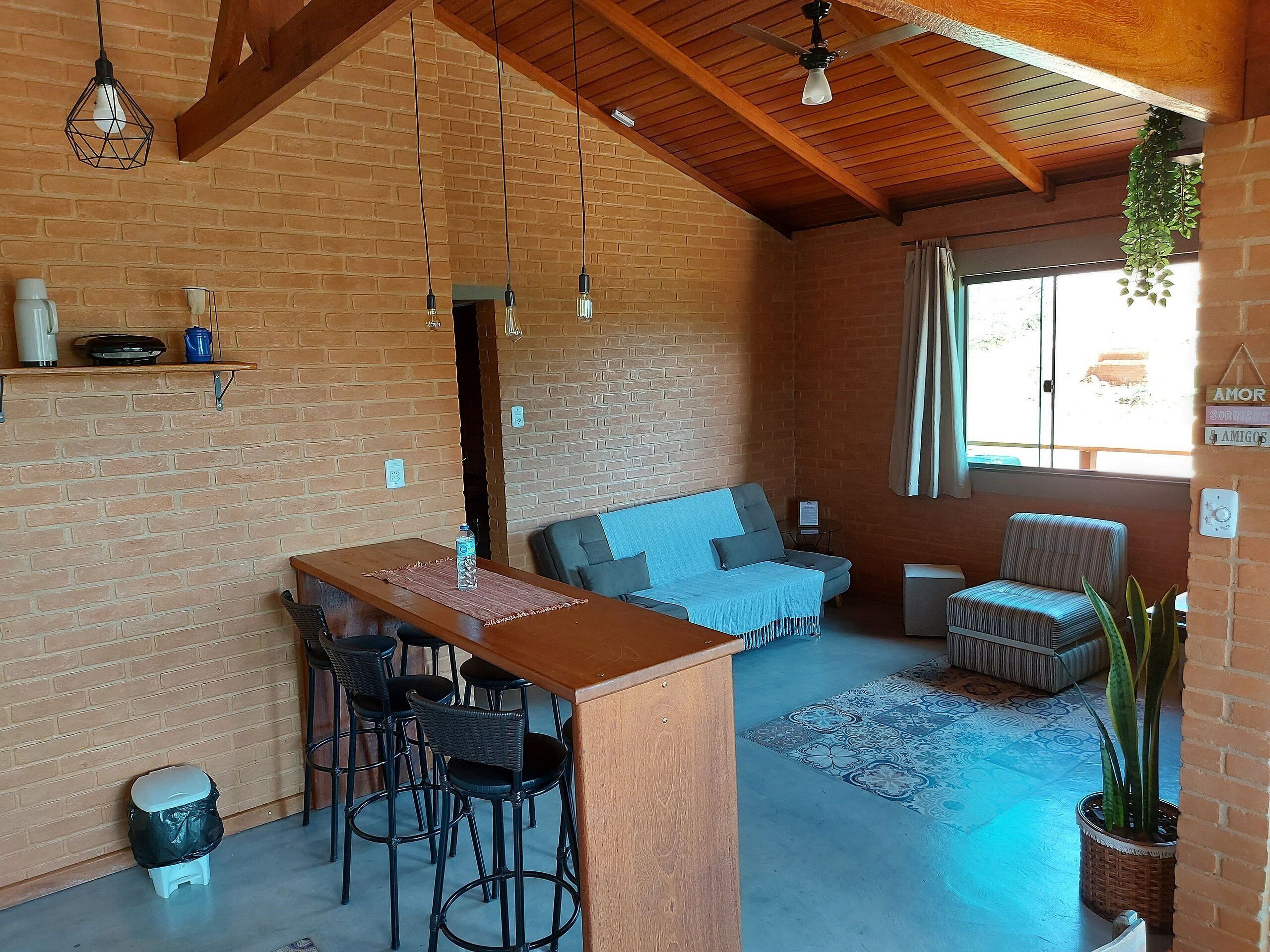 Una habitación acogedora con techo de madera, paredes de ladrillo, zona de comedor con taburetes, un sofá y una planta en maceta.
