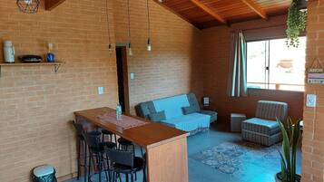 Una habitación acogedora con techo de madera, paredes de ladrillo, zona de comedor con taburetes, un sofá y una planta en maceta.