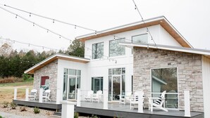 Una casa moderna de dos pisos con fachada de piedra, ventanas amplias y una terraza con mobiliario exterior.