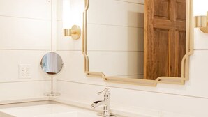 Un baño con tocador blanco, un espejo, un lavamanos y un dispensador de papel higiénico.