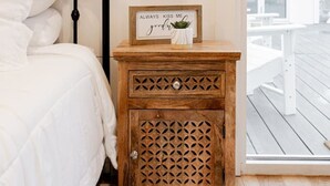 Un dormitorio con cama, una mesita de noche con un cartel enmarcado, una lámpara de pared y vistas a una terraza exterior.