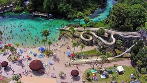 An aerial view of a beach area with a winding water slide, clear turquoise water, and people enjoying the beach and water activities. - Stay directly on crystal clear waters of Weeki Wachee River with your own beach! (weekiwachee)